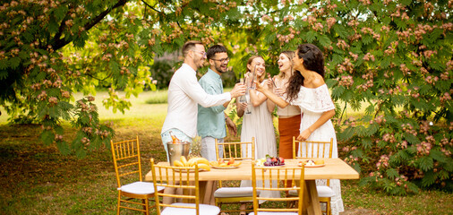Group of happy young people cheering with fresh lemonade and eating fruits in the garden