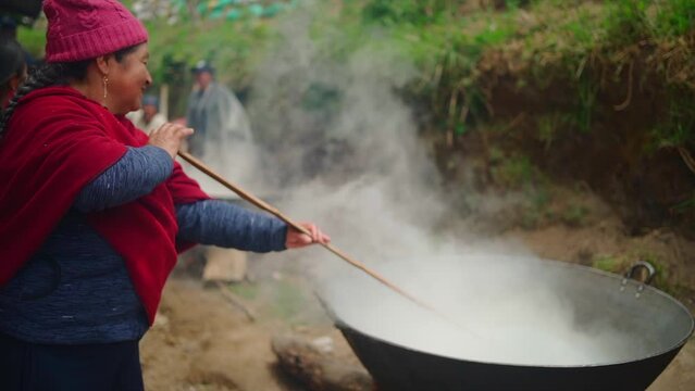 Peasant woman stirring food with stick in pot
