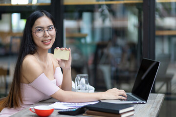 Attractive Asian woman holding a credit card and using a laptop is shopping online.