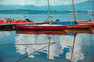 Red and yellow boats in the summer by the beach sea lake. Sunny day and clouds. Cheerful people...