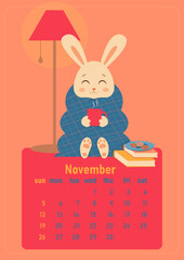 Calendar 2023 for november. Year of the rabbit, symbol of the new year. The week starts on Sunday. A cute rabbit is wrapped in a blanket and sits with a cup of hot drink at home with cookies and books