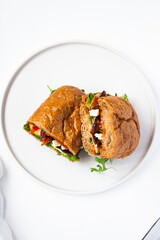 Photo of a delicious freshly made sandwich from brown bread with meat, red fish, greens, sauce, eggs, cheese and other sandwich ingredients on a white modern porcelain plate on a white background 