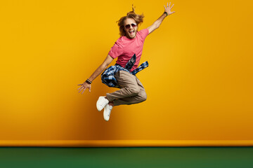 Stylish young man looking excited while jumping against yellow background