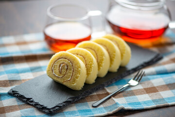 ガラス製のカップに入った紅茶とスレートプレートに乗ったロールケーキ
