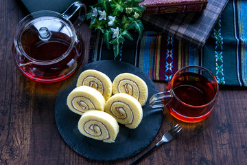 ガラス製のカップに入った紅茶とスレートプレートに乗ったロールケーキ
