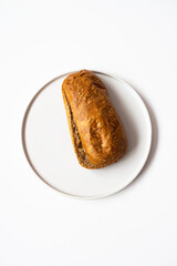 Photo of a fresh homemade delicious brown bread lying on a whit modern flat porcelain plate on a white background