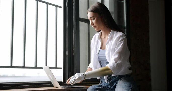 Motivated woman using prosthetic arm working or learning notebook computer, girl with disability typing text artificial prosthetic limb