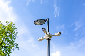 Modern lamppost and 3 surveillance cameras mounted in different directions in public park. Public space security systems