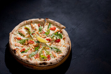 Pizza with salmon, mozzarella, cherry tomatoes, arugula, lemon and parmesan. Italian cuisine. On a black background. Free space for text. View from above.