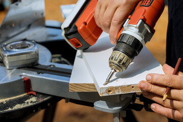 As part his construction work carpenter is drilling in wooden boards with screwdriver and connecting them