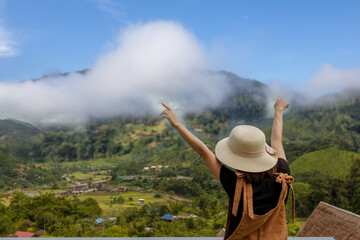 back view of woman wearing black t-shirt and hat lift smart phone up to take a photo,seeing the nature foogy over mountain,travel concept