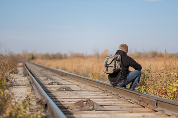 Fototapeta na wymiar a man with a backpack on his back sits on the rails. traveler on the railroad. man on rails. tourist with a backpack