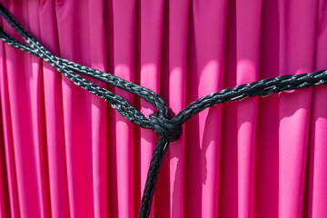 Reliable node close-up. Strong black nylon rope knotted on magenta background. Symbol of strong,...