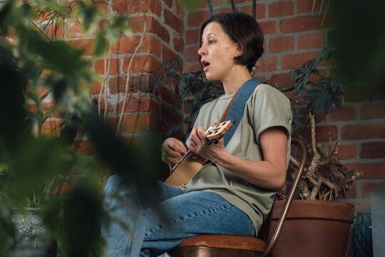 Young woman playing ukulele and singing sitting on the chair