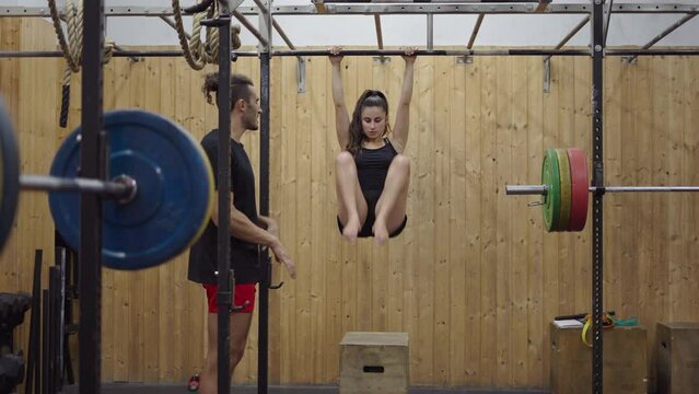 Petite woman doing pull up abdominal exercise while conversating with her personal trainer - front view 