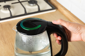 Close-up of a woman pressing the power switch on an electric kettle.Save energy at home.A modern...