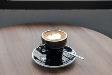 Blur,Latte coffee with heart shaped art in black cup on a wood patterned background. Close up,cup of latte coffee with a wood patterned table background. Beautyful latte art.