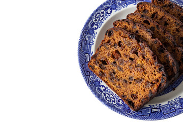 Fruit loaf cake sliced on a decorated blue and white plate.  On a white background