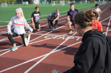 Fototapeta premium Female coach and group of children conducts a training session at the stadium. School gym trainings or athletics