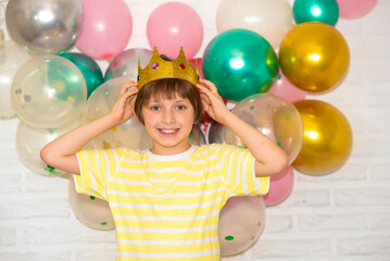 Fototapeta na wymiar a happy boy with a crown on his head stands in front of a brick wall decorated with balloons