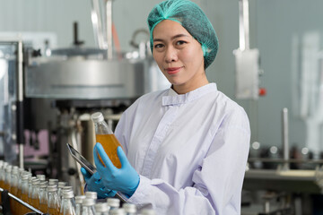Asian female manufacturer checking product bottles fruit juice on the conveyor belt in the beverage factory. Woman worker checks product bottles in beverage factory. Inspection quality control