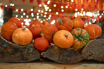 autumn harvest concept. Bunch of appetizing orange pumpkins on wood, backdrop bokeh blurred light bulbs and red flags. Festival, thanksgiving day, helloween, counter for sale, Horizontal, front view