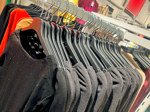 Clothes On A Rack In A Store. Wardrobe With Same Black Dresses And T-shirts. Black Women's Fashion Clothes Hanging On Hangers. Closeup On Group Of Accessory, Household Showroom Department