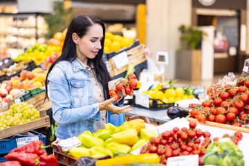 Smiling good-looking brunette checks on quality of organic red tomatoes in the market