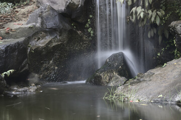 A small waterfall falls vertically into a pond.
