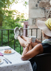 detail side view of a woman drinking coffee in peace on the terrace of her house. selective focus on the cup of coffee. concept of sunrise and breakfast in peace and quiet.