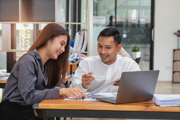 Two male and female marketers use company documents and use laptop computers to record data to analyze company profits.