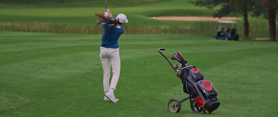 Caucasian female playing golf, striking a ball during the course