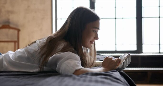 Girl with bionic arm using phone, reading social media and chatting in bed, woman with disability learning or working online remotely from home