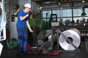 A worker in production moves workpieces for large diameter bearings. Lifting crane. Manufacture of...