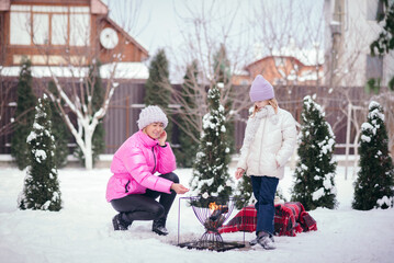 mom and daughter have fun and make a picnic in winter near the house.