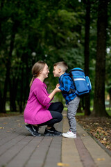 Young woman leads her excited son to first class on a sunny day. Ready to study.