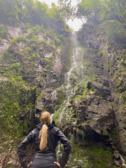 Blond woman standing in front of waterfall in rainy black forest, Germany