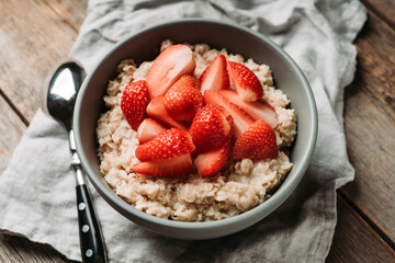 Oatmeal with red ripe strawberries and honey in the bowl. Selective focus.
