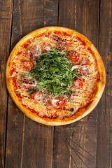 Pizza with tomato, meat and arugula. On a wooden table.