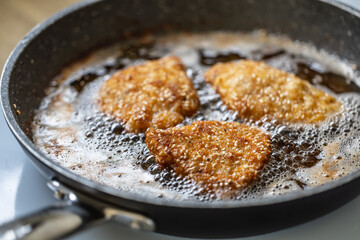 Breaded schnitzels are frying in a sizzling pan making the traditional vienese food