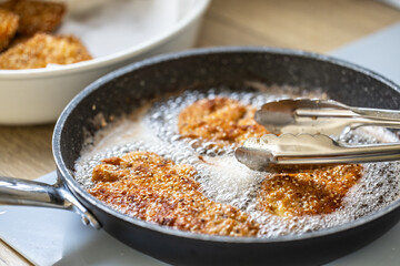 Detail of pan with schnitzels bubbling in hot oil and pliers taking them out
