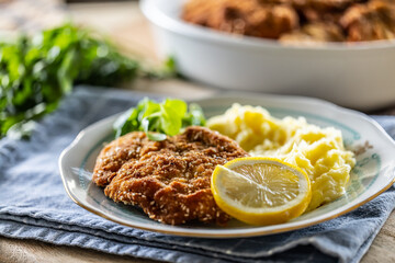 Breaded meat served with potato mash, slice of lemon and greens