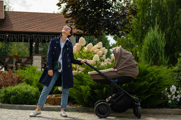 Young mother in a coat walks with a stroller. Stylish woman in new glasses for vision.