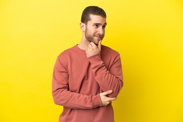 Handsome blonde man over isolated yellow background thinking an idea while looking up