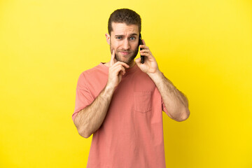 Handsome blonde man using mobile phone over isolated background having doubts while looking up