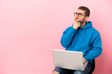 Young man sitting on a chair with laptop having doubts and with confuse face expression