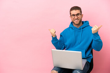 Young man sitting on a chair with laptop with thumbs up gesture and smiling