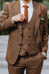 Close-up portrait of the groom in a brown, expensive, stylish suit with a boutonniere, tie and a...