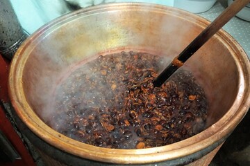 Großer Kupferkessel mi dampfendem heißen Muhs und Rührstab aus Holz in Waschküche auf Bauernhof...