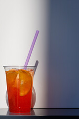 refreshing summer cocktail. A cold orange drink in a takeaway glass against a wall background. Sale of summer drinks lifestyle